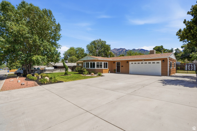 6889 South Village Road Salt Lake City, UT 84121 - Photo 2 of 44 Single-story residence featuring a two-car garage with a white sectional door, a concrete driveway, and established front landscaping