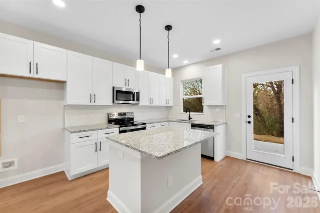 a kitchen with stainless steel appliances granite countertop a stove top oven a sink a refrigerator and white cabinets with wooden floor