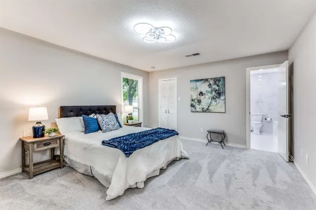 a spacious bedroom with a bed and a lamp on dresser