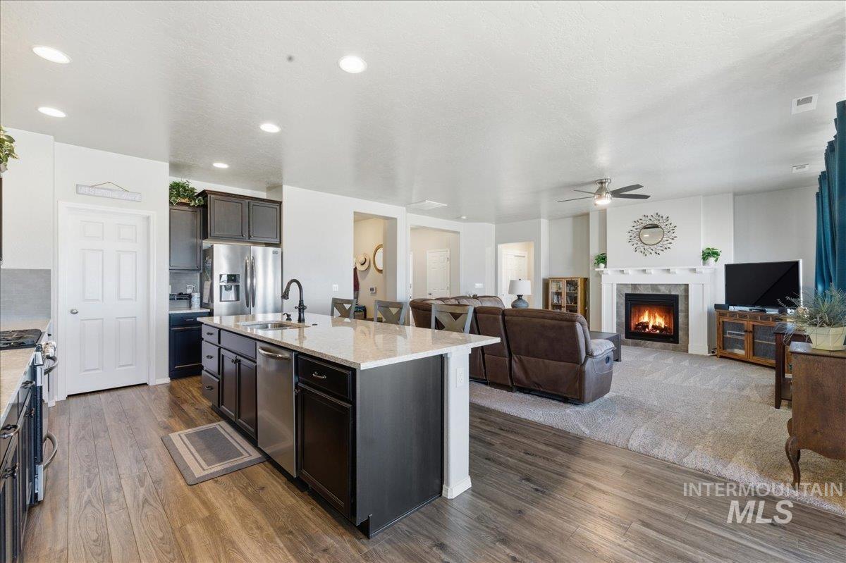 16202 Dietz Way Caldwell, ID 83607 - Photo 30 of 31 Kitchen featuring a warm lit fireplace, dark wood-type flooring, open floor plan, light stone counters, and stainless steel appliances