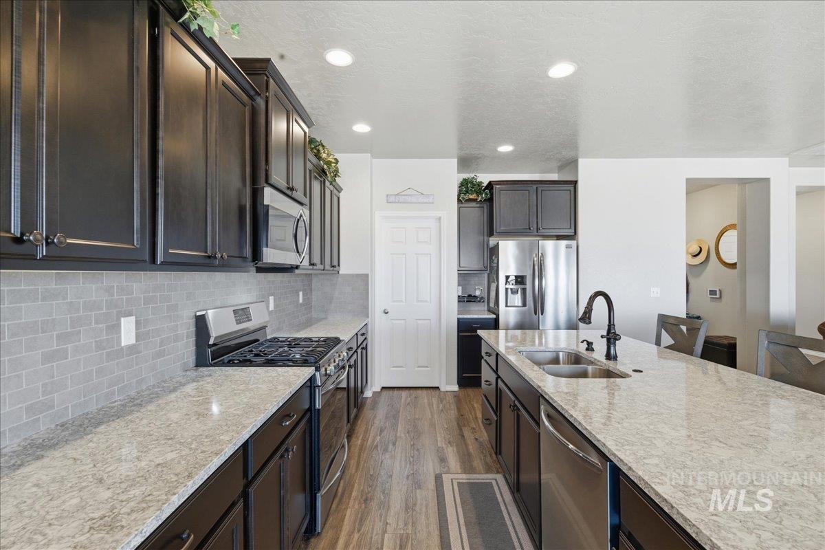 16202 Dietz Way Caldwell, ID 83607 - Photo 7 of 31 Kitchen featuring stainless steel appliances, dark wood finished floors, light stone counters, dark wood finish cabinets, and decorative backsplash