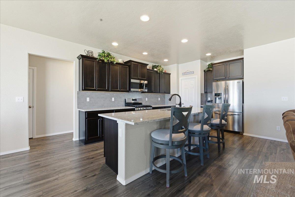 16202 Dietz Way Caldwell, ID 83607 - Photo 8 of 31 Kitchen with stainless steel appliances, dark wood finish cabinets, dark wood-style floors, a kitchen bar, and a kitchen island with sink