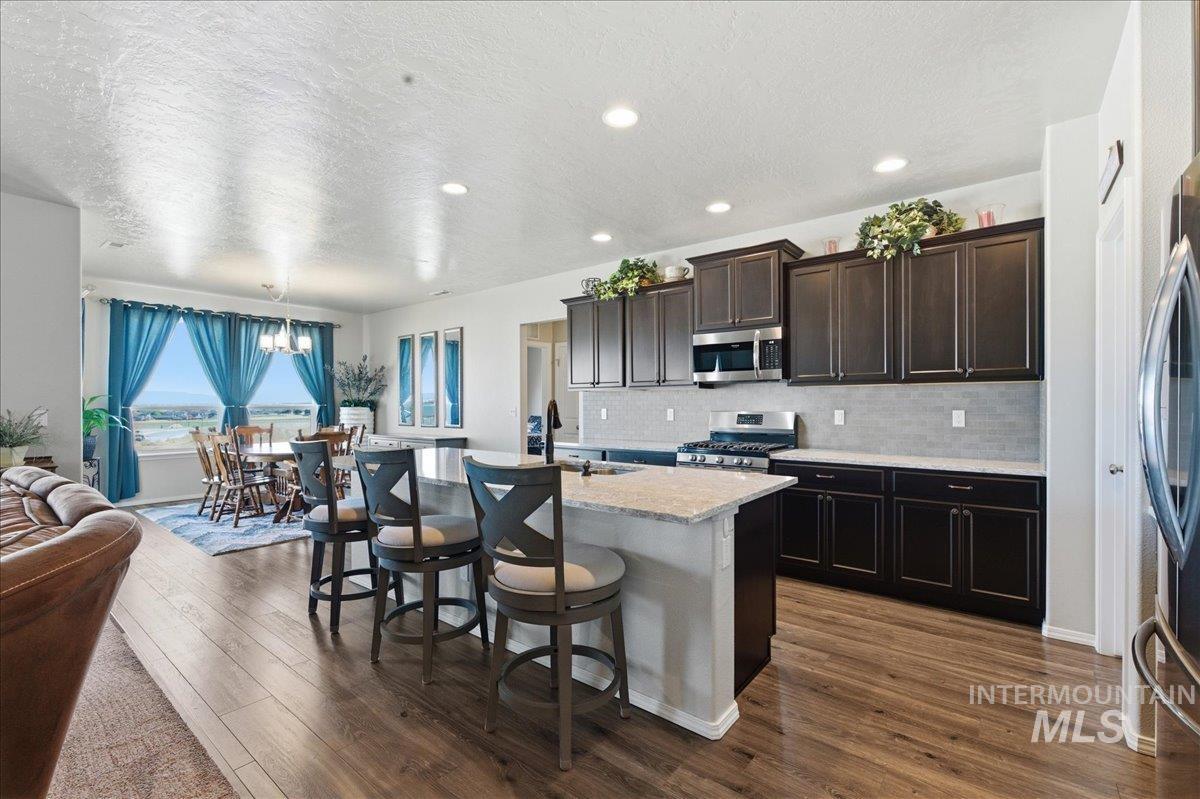 16202 Dietz Way Caldwell, ID 83607 - Photo 9 of 31 Kitchen with dark wood finish cabinets, a kitchen breakfast bar, an island with sink, stainless steel appliances, and a textured ceiling