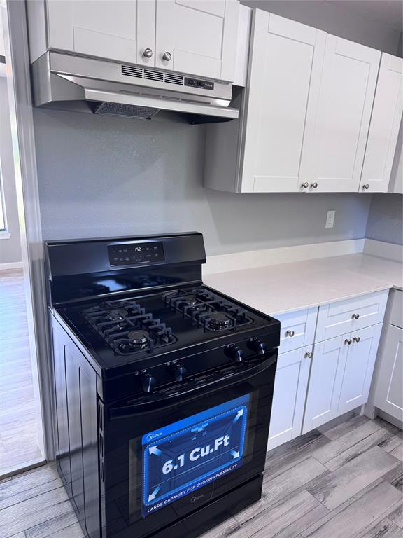 1736 Ransom Terrace Fort Worth, TX 76112 - Photo 4 of 27 Modern kitchen featuring a black gas range, white shaker-style cabinetry with silver hardware, stone-finish countertops, stainless steel range hood, and wood-finish flooring