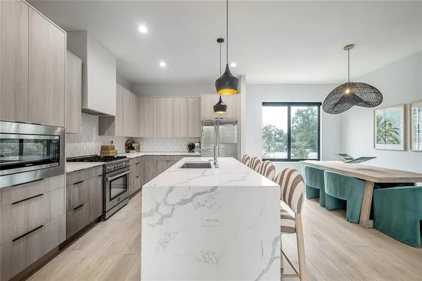 a kitchen with stainless steel appliances granite countertop a stove a sink a refrigerator and a dining table with wooden floor