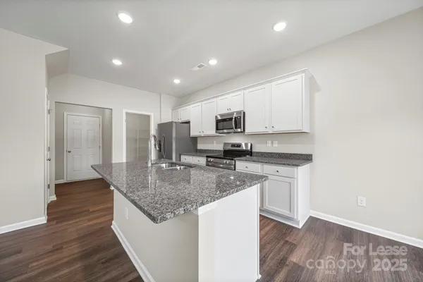 a kitchen with stainless steel appliances granite countertop a sink dishwasher a microwave oven and a refrigerator with wooden floor