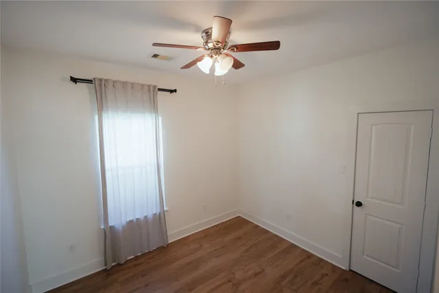 a view of an empty room with wooden floor and a ceiling fan