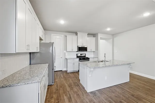 a kitchen with stainless steel appliances granite countertop a sink dishwasher a refrigerator and white cabinets with wooden floor