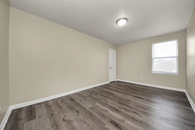 a view of an empty room with wooden floor and window