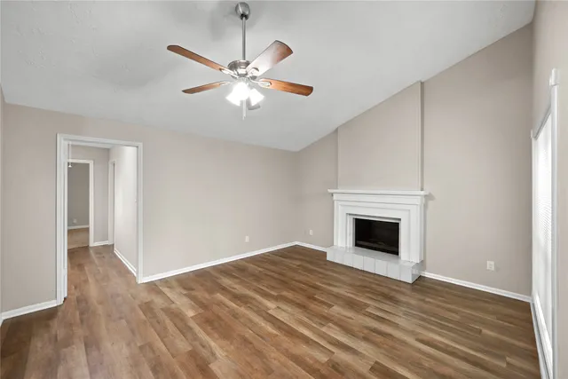 a view of an empty room with wooden floor fireplace and a window