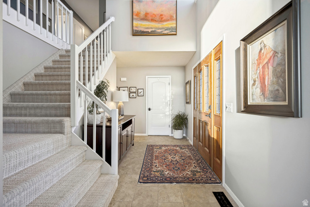 1837 Richard Road Sandy, UT 84093 - Photo 19 of 67 Two-story foyer featuring a grand staircase with carpeted treads, white painted balusters and railings, a wood-finish entry door with leaded glass panels, high ceilings, and neutral-toned tile flooring