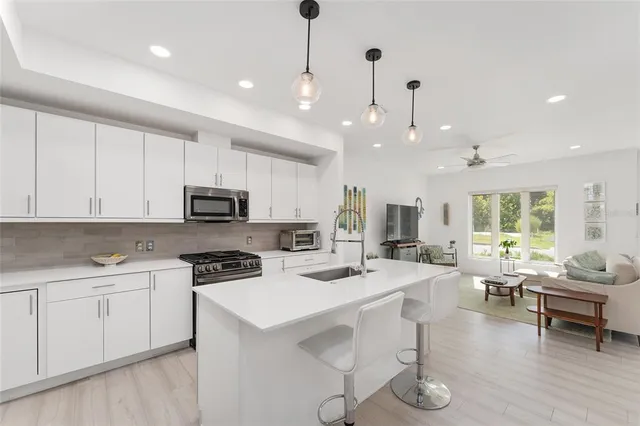 a kitchen with stainless steel appliances kitchen island granite countertop a stove a sink a refrigerator and white cabinets with wooden floor