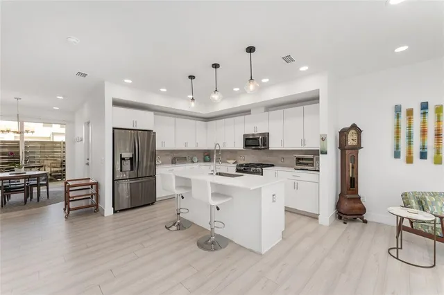 a kitchen with stainless steel appliances a refrigerator a stove top oven a sink dishwasher and white cabinets with wooden floor