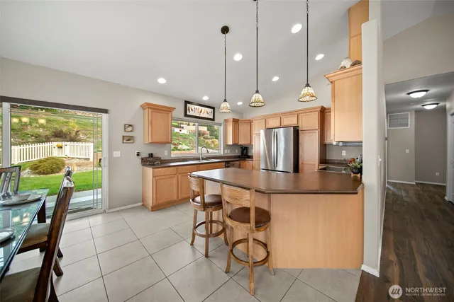 a kitchen with stainless steel appliances kitchen island granite countertop a refrigerator a stove a sink a dining table and chairs with wooden floor