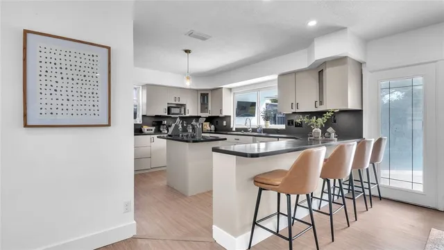 a kitchen with stainless steel appliances granite countertop a stove a sink a refrigerator white cabinets and couches with wooden floor