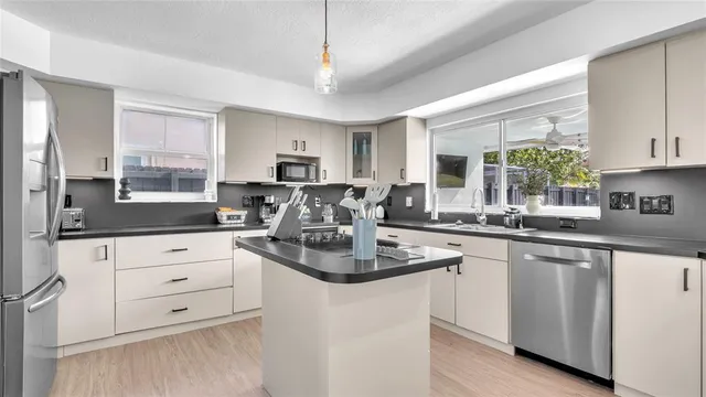 a kitchen with stainless steel appliances granite countertop a stove a sink dishwasher a refrigerator and white cabinets with wooden floor