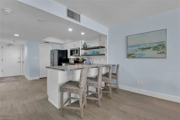 a kitchen with stainless steel appliances kitchen island granite countertop a dining table chairs and a refrigerator
