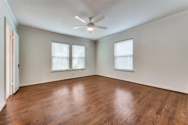 an empty room with wooden floor chandelier fan and windows