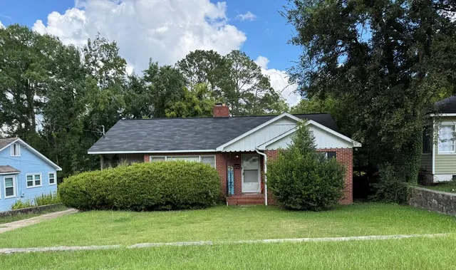 a view of a house with a yard plants and large tree