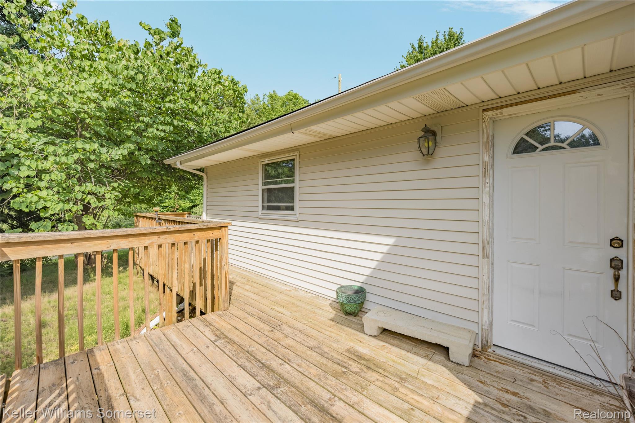 2344 Rochester Road Leonard, MI 48367 - Photo 50 of 66 Expansive wood deck with natural wood railings, featuring a side entrance door with an arched window and an exterior wall lantern
