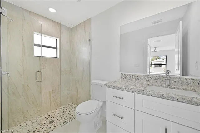 a bathroom with a granite countertop sink a toilet a mirror and shower