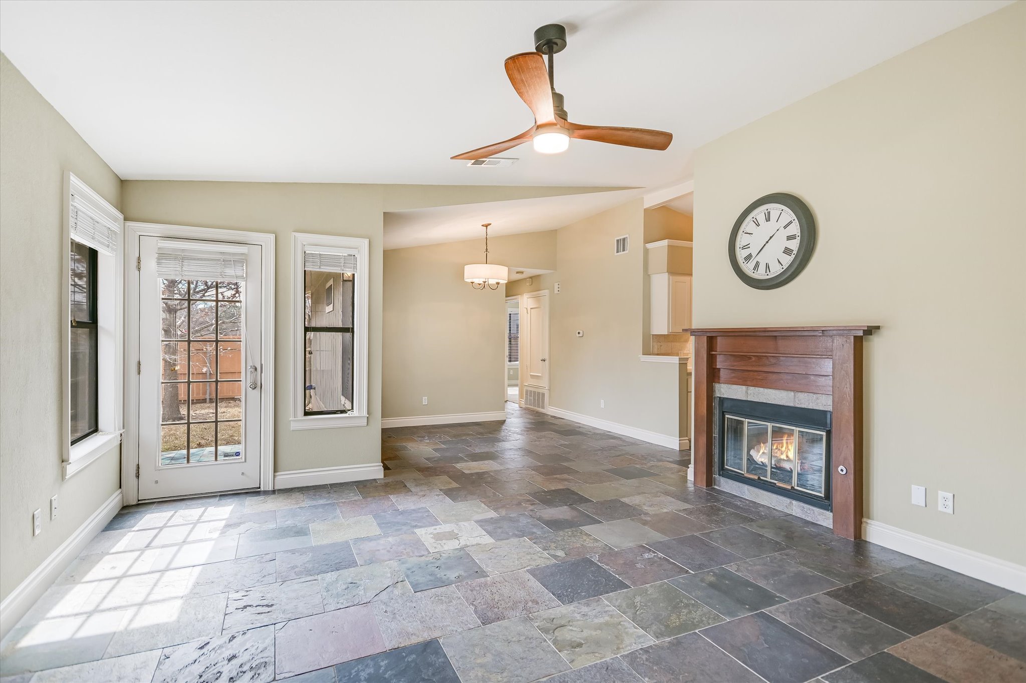 7701 Grovedale Trail Austin, TX 78729 - Photo 3 of 13 Unfurnished living room featuring a ceiling fan, stone tile floors, a glass covered fireplace, and vaulted ceiling