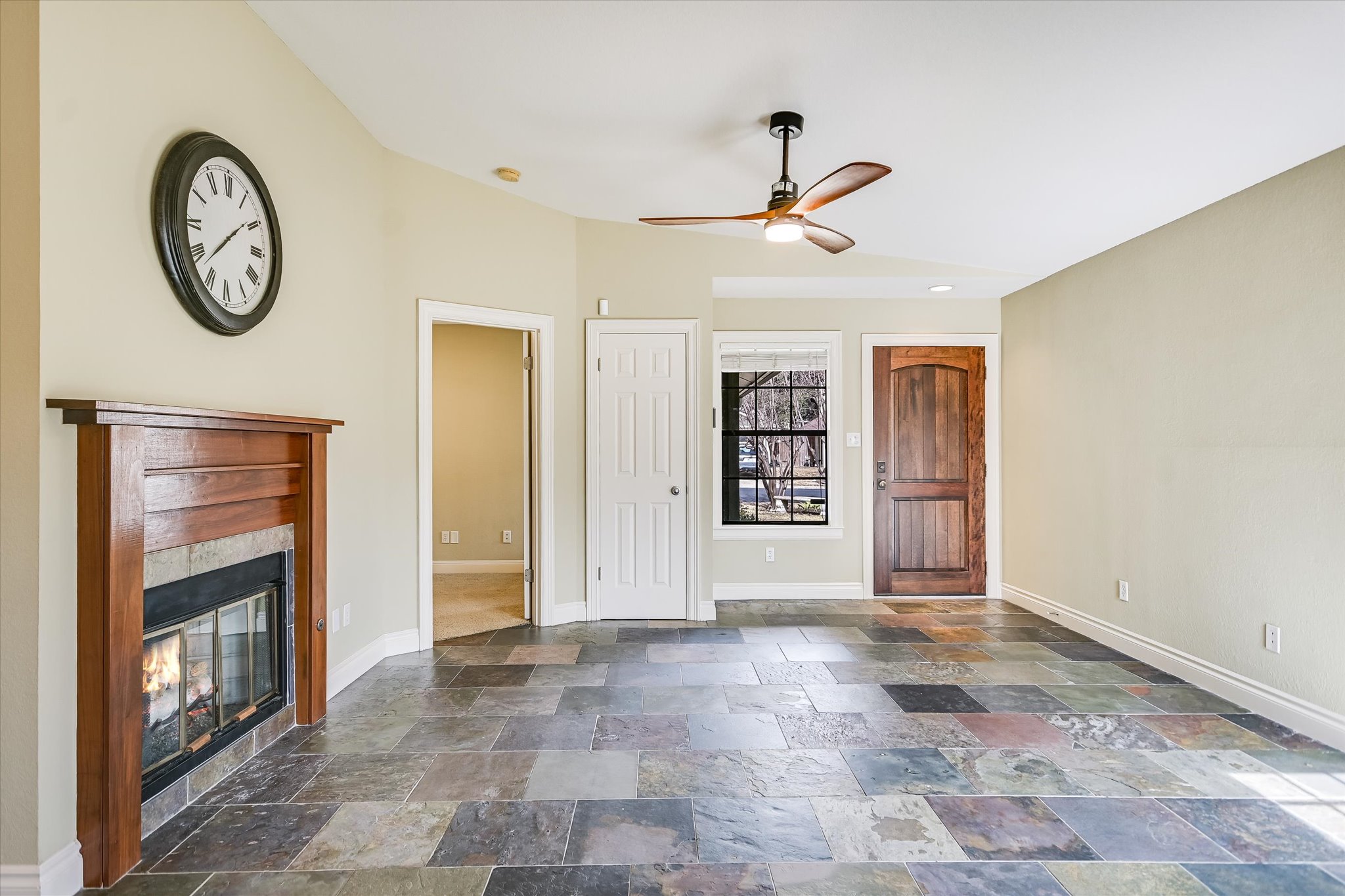 7701 Grovedale Trail Austin, TX 78729 - Photo 4 of 13 Unfurnished living room featuring ceiling fan, dark stone finish flooring, and a fireplace