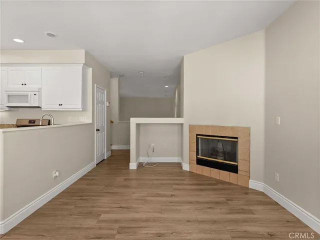 a view of empty room with wooden floor and kitchen