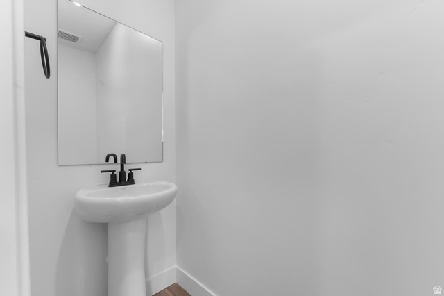 342 North Rhyolite Drive, Unit 88 Hurricane, UT 84737 - Photo 11 of 26 Modern pedestal sink with matte black faucet, wall-mounted mirror, white walls, and wood-finish flooring