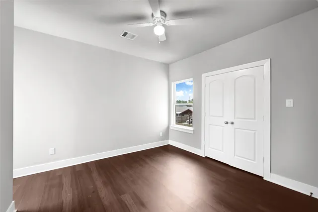 an empty room with wooden floor chandelier fan and windows