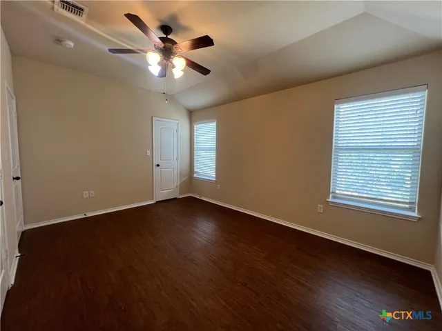 a view of an empty room with wooden floor and a ceiling fan