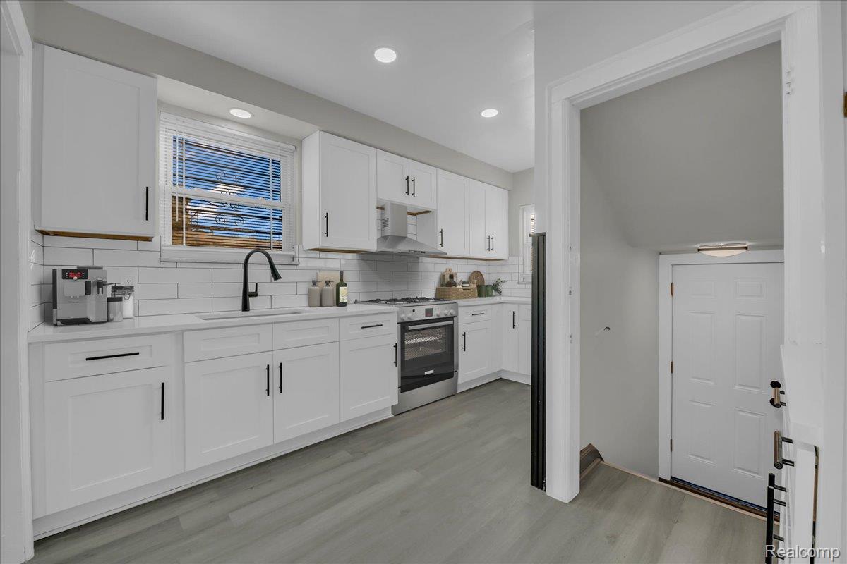 16717 Fielding Street Detroit, MI 48219 - Photo 16 of 46 Kitchen with white cabinetry, backsplash, stainless steel range with gas cooktop, light wood-style floors, and recessed lighting
