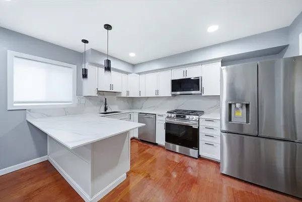 a kitchen with stainless steel appliances a stove a sink a refrigerator white cabinets and wooden floor