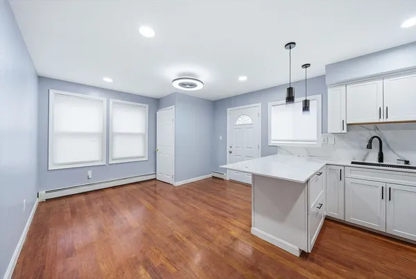 a kitchen with granite countertop a stove a sink and white cabinets with wooden floor