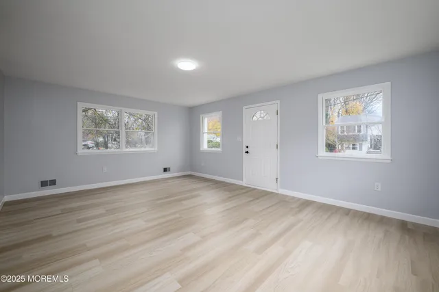 a view of an empty room with a window and wooden floor