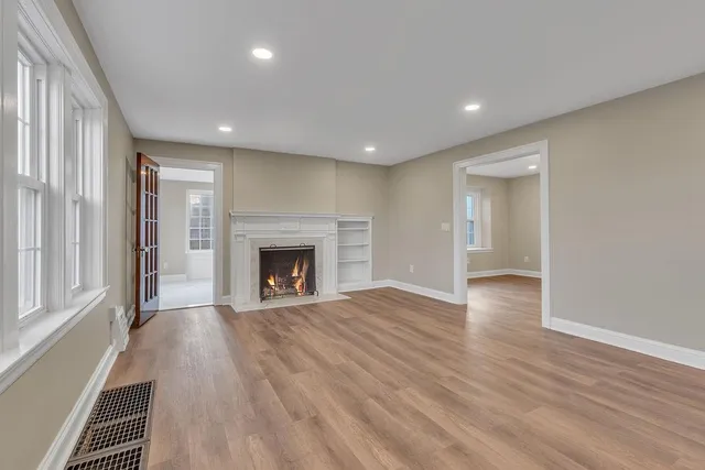 an empty room with wooden floor fireplace and windows