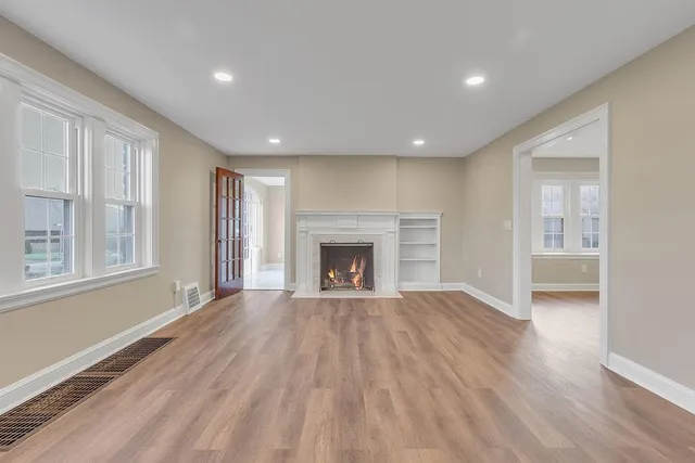 a view of an empty room with wooden floor fireplace and a window