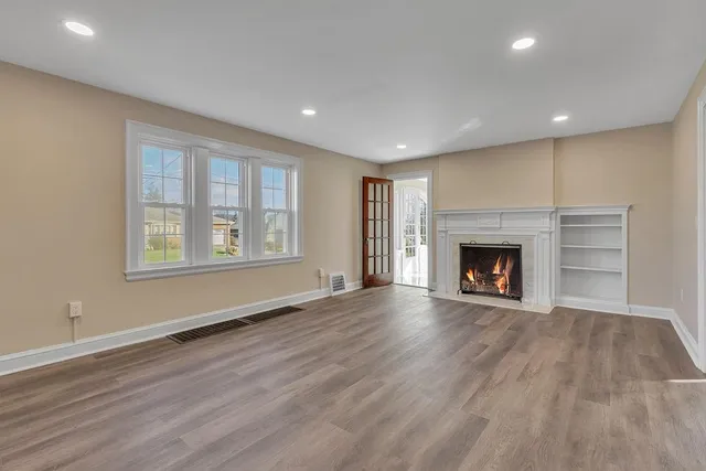 an empty room with wooden floor fireplace and windows