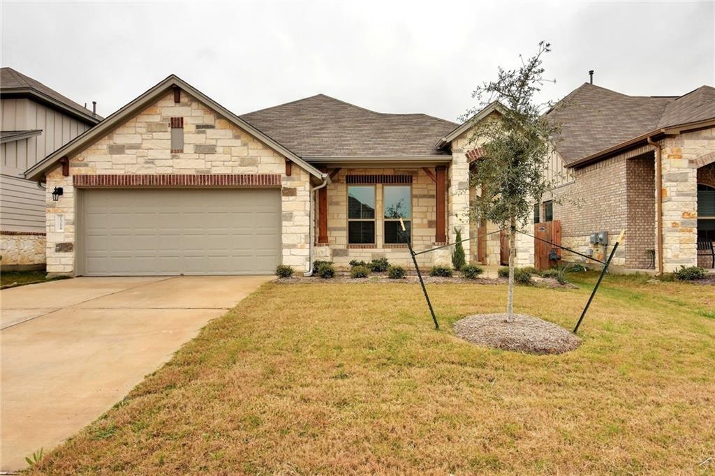View of front of house featuring stone siding, a shingled roof, concrete driveway, an attached garage, and a front lawn