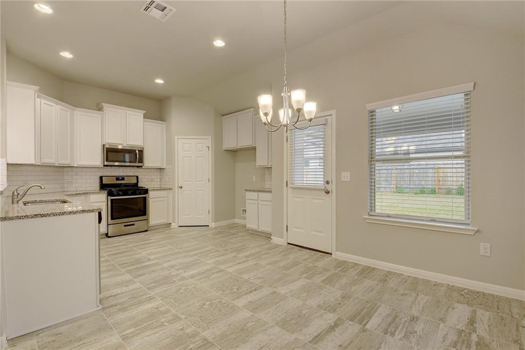 13216 Mariscan Street Manchaca, TX 78652 - Photo 6 of 28 Kitchen with stainless steel appliances, white cabinetry, a chandelier, light stone counters, and backsplash