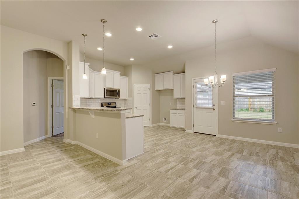 13216 Mariscan Street Manchaca, TX 78652 - Photo 7 of 28 Kitchen with white cabinetry, a kitchen bar, a peninsula, arched walkways, and stainless steel appliances