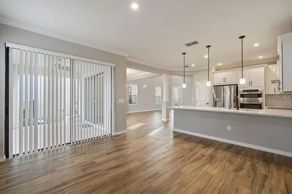 a living room with stainless steel appliances wooden floors and kitchen view