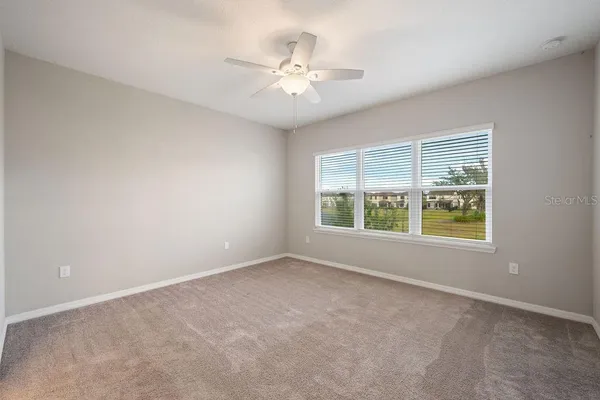 an empty room with a chandelier fan and windows