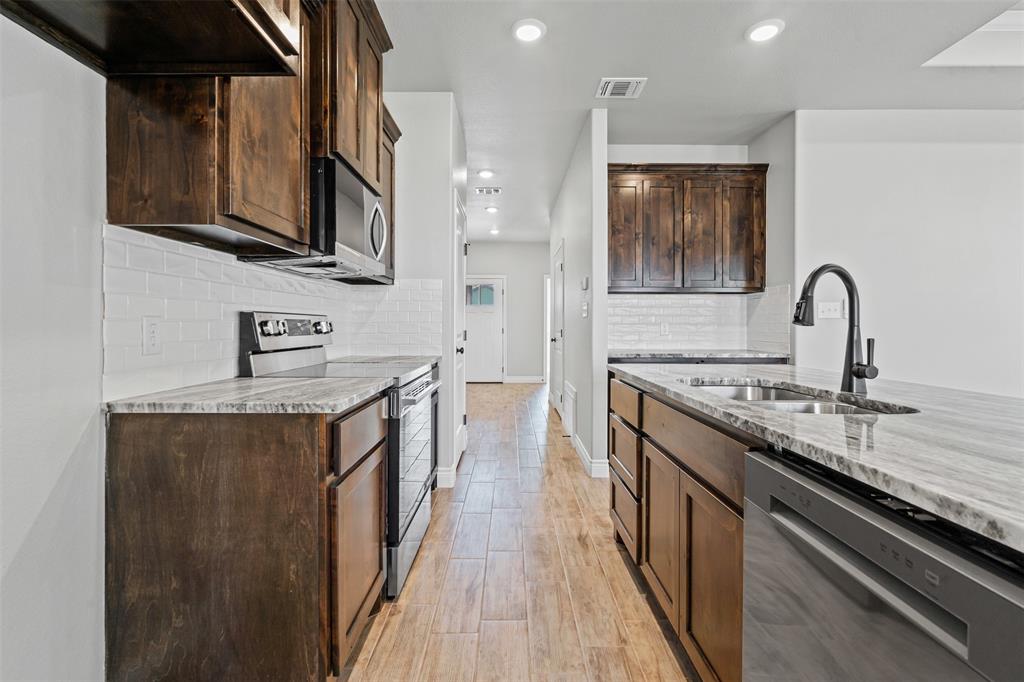 3400 Hilltop Road Granbury, TX 76048 - Photo 18 of 40 a kitchen with stainless steel appliances granite countertop a stove top oven a sink dishwasher and wooden cabinets with wooden floor
