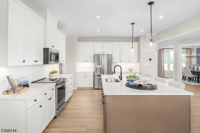 a open kitchen with stainless steel appliances granite countertop a stove a sink a refrigerator and white cabinets with wooden floor