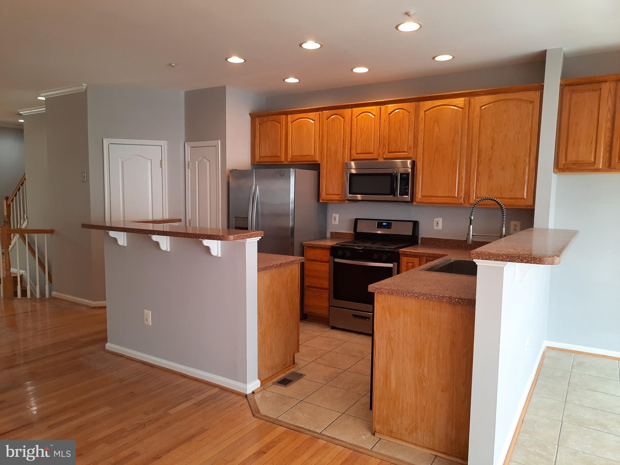 10258 Rutland Round Road, Unit 13 Columbia, MD 21044 - Photo 8 of 46 a kitchen with stainless steel appliances granite countertop a refrigerator a stove a sink and a microwave with wooden floor
