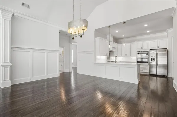 a view of an empty room and kitchen with wooden floor