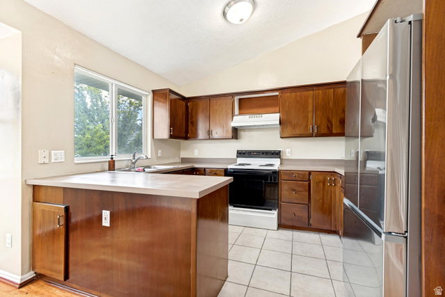 843 Deer Flat Road Tooele, UT 84074 - Photo 9 of 27 U-shaped kitchen featuring wood cabinetry, a white stove with a range hood, and a stainless steel refrigerator