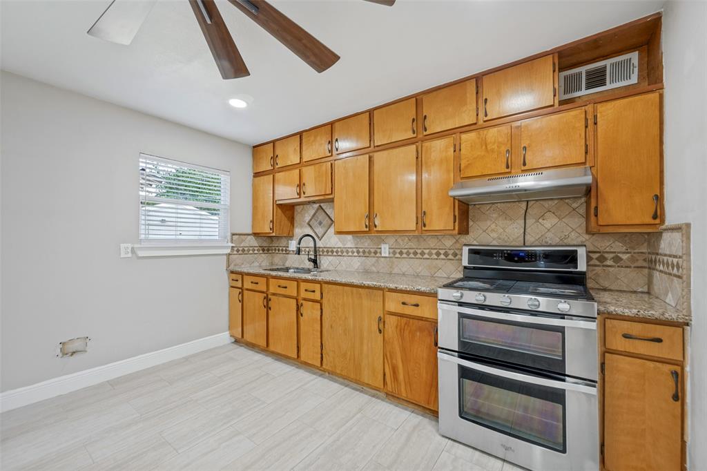 3584 Regal Road Fort Worth, TX 76111 - Photo 6 of 12 Wood-finish cabinetry paired with granite-style countertops and a decorative tile backsplash