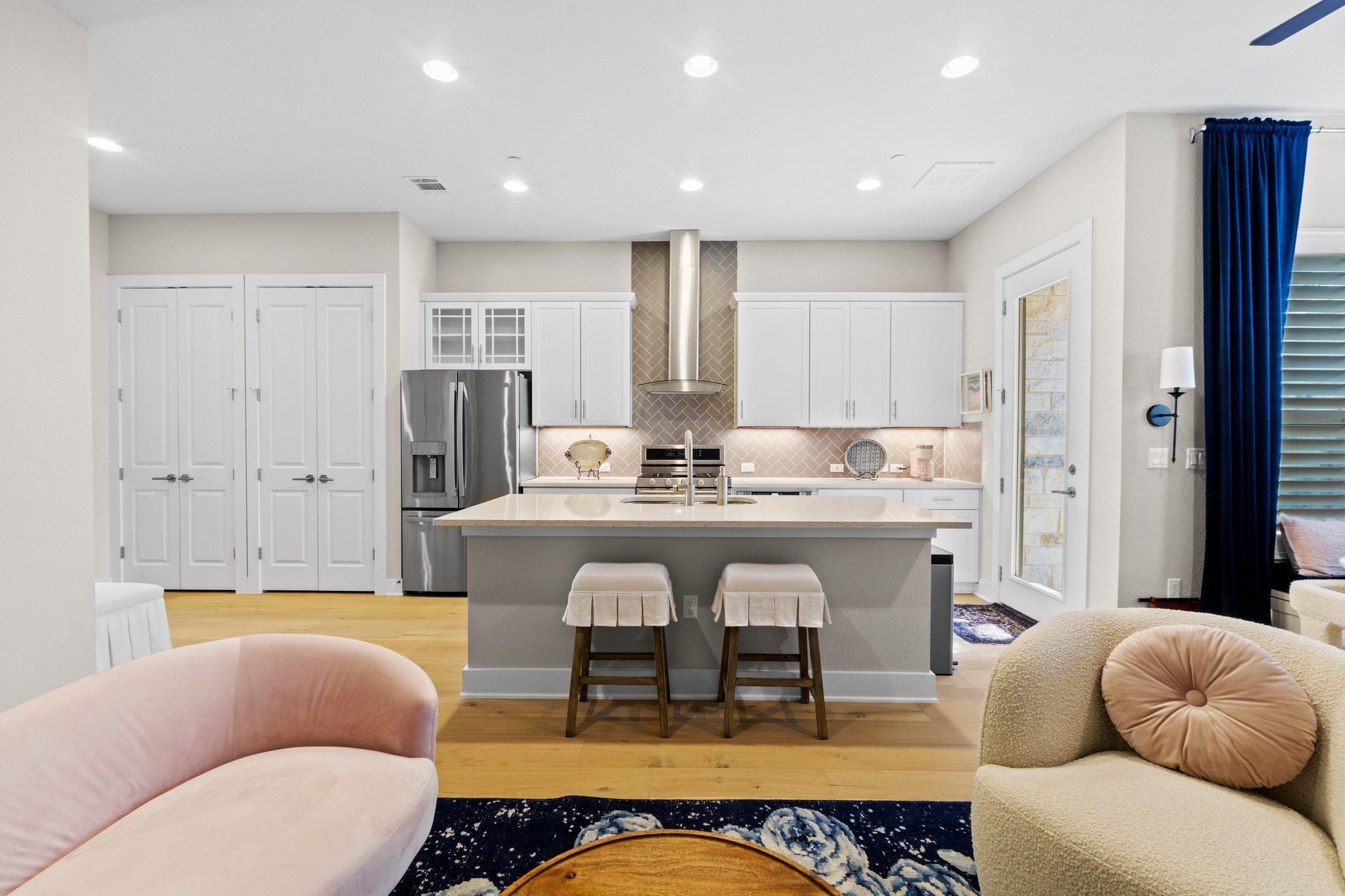 Kitchen featuring a kitchen island with sink, white cabinetry, stainless steel fridge, a breakfast bar, and recessed lighting